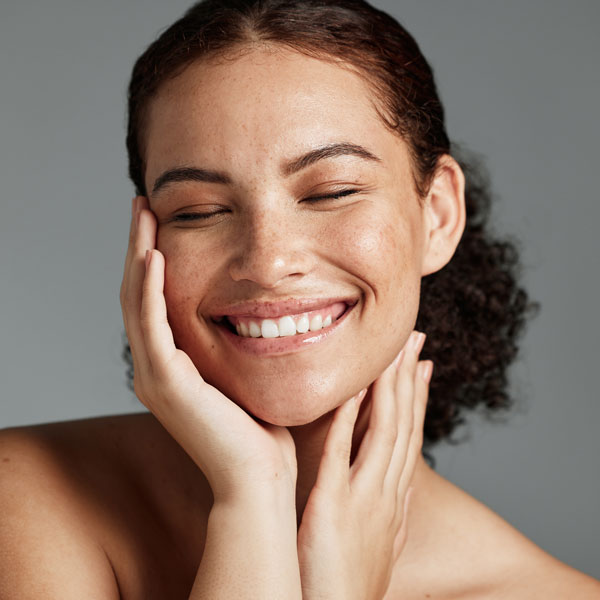 woman smiling and touching her glowing skin